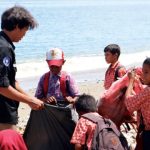Mahasiswa IPB dari Himiteka mengajak anak murid SD Alhilaal Wamlana Pulau Buru, Maluku memungut sampah di Pantai Wamlana. Foto: Berita IPB
