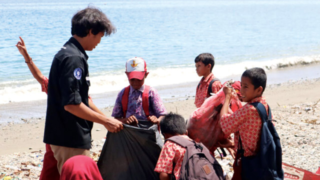 Mahasiswa IPB dari Himiteka mengajak anak murid SD Alhilaal Wamlana Pulau Buru, Maluku memungut sampah di Pantai Wamlana. Foto: Berita IPB